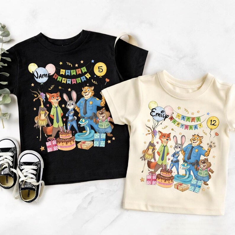 K&ouml;nnte beinhalten: Zwei kurz&auml;rmelige T-Shirts, eines in Schwarz und eines in Creme, mit einem farbenfrohen Cartoon-Design mit Figuren, einer Geburtstagstorte und dem Schriftzug "Happy Birthday". Das schwarze Shirt hat den Namen "Jame" und die Zahl "5", das cremefarbene Shirt hat "Emily" und die Zahl "12".