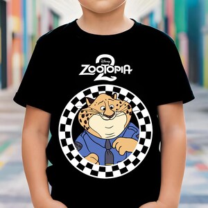May include: Black t-shirt with the "Zootopia 2" logo and a cartoon cheetah in a police uniform. The cheetah is inside a black and white chequered circle. The t-shirt is worn by a child.