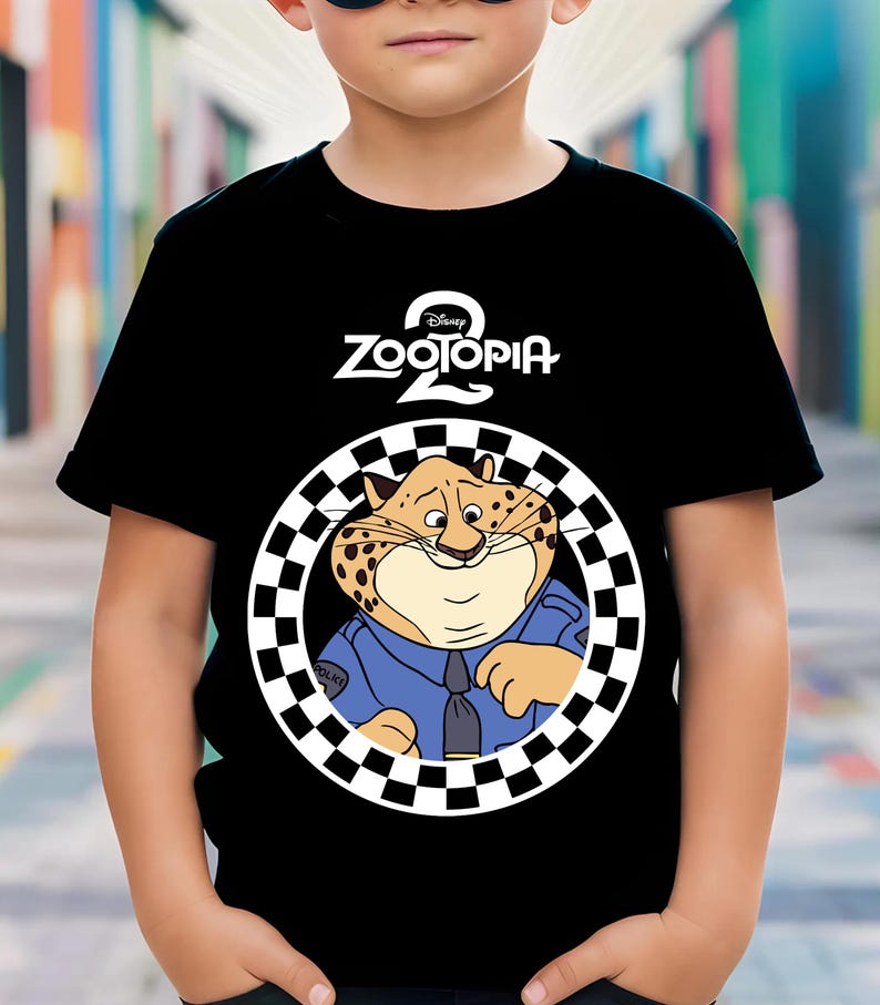 May include: Black t-shirt with the "Zootopia 2" logo and a cartoon cheetah in a police uniform. The cheetah is inside a black and white chequered circle. The t-shirt is worn by a child.