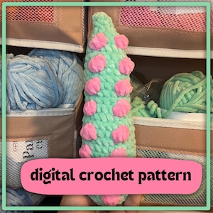 May include: A handmade, cone-shaped crochet item in light green with pink accents. The text "digital crochet pattern" is displayed on a pink banner. The background shows various yarn colors, suggesting a crafting theme.