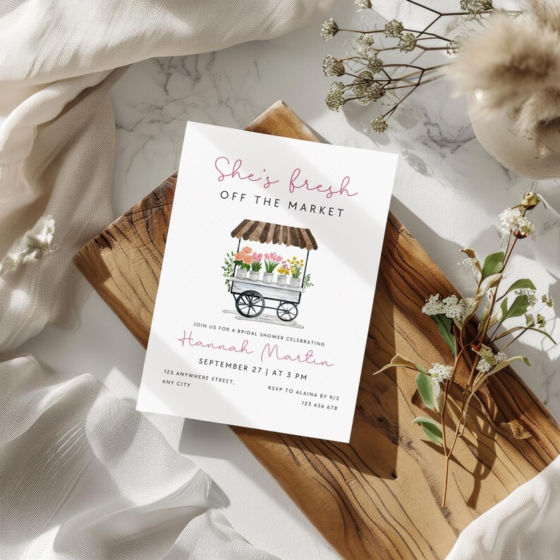 Peut inclure: Une carte blanche avec une illustration florale d'un chariot &agrave; fleurs avec le texte "She's fresh off the market" et le texte "Join us for a bridal shower celebrating Hannah Martin September 27 at 3 PM 123 Anywhere Street, Any City RSVP to Alaina by 9/3 123 456 678"