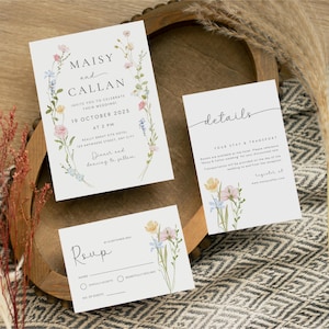 May include: A wedding invitation suite with floral designs. The main invitation features a wreath of watercolor flowers with the names Maisy and Callan, the wedding date, and the location. The RSVP card has a floral design and space for guests to indicate their attendance. The details card has a floral design and information about the wedding, including the hotel and transportation.