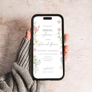 May include: A smartphone displays a bridal shower invitation. The invitation features floral accents in pink, blue, and yellow, with the text "BRIDAL shower honoring Hannah Brown." The date is Saturday, November 6, at one o'clock in the afternoon.