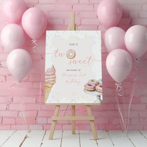 May include: A wooden easel holds a pink and white sign with the text "She's Two Sweet" and "Welcome to Harper's 2nd Birthday." The sign includes illustrations of a donut, ice cream cone, and donuts. Pink balloons are arranged around the easel.