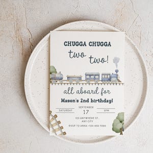 May include: A birthday invitation with a train theme. The invitation reads "CHUGGA CHUGGA two two!" and "all aboard for Mason's 2nd birthday!" Includes date, time, and RSVP information. The invitation is on a white plate.