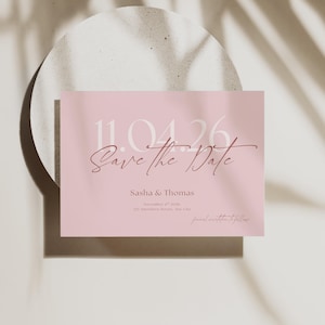 Puede incluir: Tarjeta "Save the Date" rosa pálido con tipografía elegante. La tarjeta presenta la fecha "11.04.26" en negrita, con las palabras "Save the Date" en escritura cursiva. También se incluyen los nombres "Sasha & Thomas".