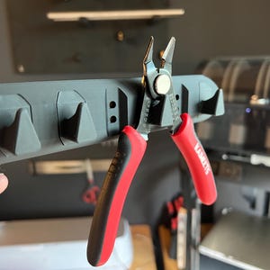May include: Red and black wire cutters with a black handle and the word "KAIETS" printed on the handle. The cutters are hanging on a black tool holder with multiple hooks.