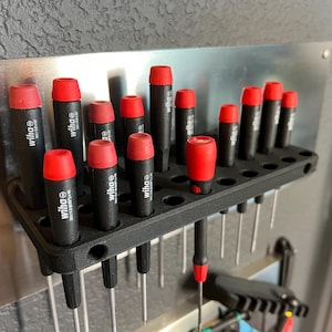 May include: A black plastic wall-mounted screwdriver holder with 18 red and black screwdrivers. The holder has a row of holes for each screwdriver. The screwdrivers are labeled "wiha" in white lettering.