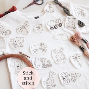 May include: White t-shirt with iron-on embroidery patches of animals and vehicles. Embroidery floss, scissors, and a wooden embroidery hoop are also present. The text "Stick and stitch" is on a pink circle.
