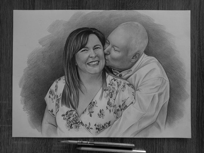 May include: A graphite pencil drawing on paper depicting a smiling person with shoulder-length hair wearing a floral print top, being kissed on the cheek by a bald person wearing a collared shirt. The artwork features detailed shading.