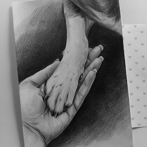 May include: A graphite pencil drawing on paper depicting a human hand gently holding an animal paw. The artwork features detailed shading and textures, rendered in monochrome tones. The composition focuses on the connection between the hand and the paw, with a dark background and a small section of patterned paper with heart icons visible on the right side.
