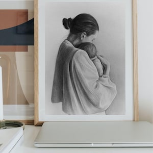 May include: A black and white charcoal drawing in a light wood frame depicting a person with hair in a bun holding a small infant close to their chest. The person wears a long-sleeved garment with gathered cuffs, and the infant is cradled securely.