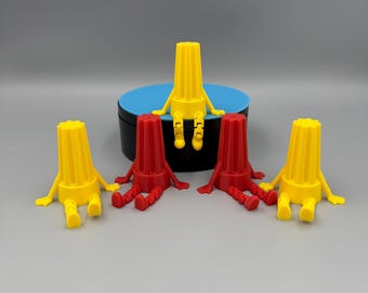 May include: Five small figurines, four are sitting on a blue surface. Two are yellow and two are red. The figurines are shaped like people with arms and legs.