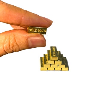 May include: Several small gold bars, each stamped with "GOLD 999.9". One bar is held between fingers, while others are stacked in a pyramid shape. The bars have a shiny, reflective surface.