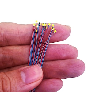 May include: A bundle of small, white LED lights with red and blue wires. The lights are arranged in a fan shape and are held in a person's hand.