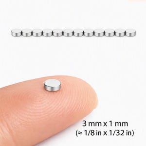 May include: A row of twelve small, circular, silver-colored metal magnets. A single matching magnet is shown resting on a fingertip for scale. The text indicates the dimensions are 3 mm x 1 mm, which is approximately 1/8 inch x 1/32 inch.