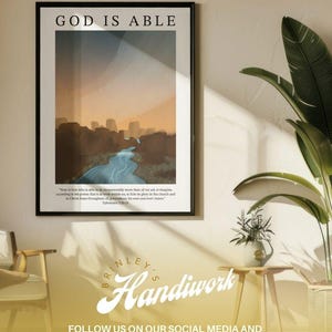 May include: Framed art print with the text "GOD IS ABLE" above a landscape illustration featuring a river and mountains. The print includes a Bible verse and the artist's name, "BRINLEY'S Handiwork", with social media information.