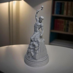 May include: A white, 3D printed sculpture of a man holding a hammer, standing on a rocky base. The sculpture is on a white surface.