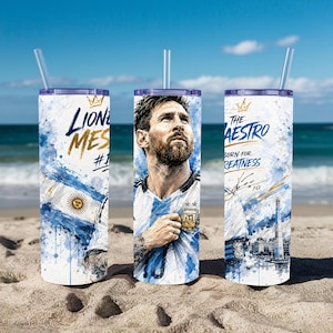 May include: A cylindrical tumbler with a clear straw featuring a graphic of Lionel Messi in an Argentina jersey, blue and white watercolor splashes, the text "Lionel Messi #10", "The Maestro", "Born for Greatness", and a signature with the number 10.