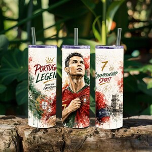 May include: A cylindrical tumbler with a metal straw featuring a portrait of a soccer player in a red jersey, the text "PORTUGAL LEGEND BORN FOR GREATNESS", the Portuguese flag, the number "7", "CHAMPIONSHIP SPIRIT", a signature, and a building illustration.