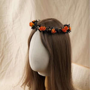 Könnte beinhalten: Ein floraler Kranz mit orangefarbenen Rosen und dunkelgrünen Blättern. Die Rosen sind um den Kranz angeordnet und bilden ein festliches und dekoratives Kopfstück. Der Kranz wird auf einem Schaufensterkopf mit braunem Haar präsentiert.
