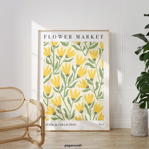 May include: A framed print with a yellow floral pattern on a cream background. The print has the text "FLOWER MARKET" at the top and "BOTANICAL COLLECTION No.1" at the bottom. The print is in a wooden frame and is hanging on a white wall.