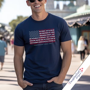 May include: A navy blue t-shirt with a red, white, and blue American flag design. The flag design includes the text "We hold these truths to be self-evident, that all men are created equal, that they are endowed by their Creator with certain unalienable Rights, that among men, deriving their just powers from the consent of the governed..." and "Independent Since 1776".