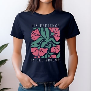 High-quality soft-style t-shirt made with ethically grown cotton. Beautiful floral graphic with a stylish font that says His presence is all around. Available in various colors. Female model wears navy.