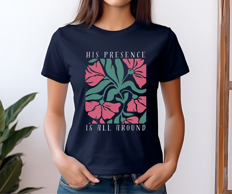 High-quality soft-style t-shirt made with ethically grown cotton. Beautiful floral graphic with a stylish font that says His presence is all around. Available in various colors. Female model wears navy.