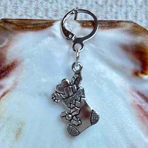 Peut inclure: Un charm de Noël argenté en forme de chaussette, orné d'un sucre d'orge, d'un cadeau et de houx. Le charm est attaché à un crochet d'oreille argenté. Le charm est probablement en métal et est conçu pour les fêtes.