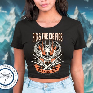 May include: Black crop top with a graphic of a skull with flames and wings. The text "FIG & THE CIG FIGS" is above the skull and "BAD KIDS TOUR" is below the skull. The text "STLVALVE BASTION CITY ELMYVILLE" is below the tour name.