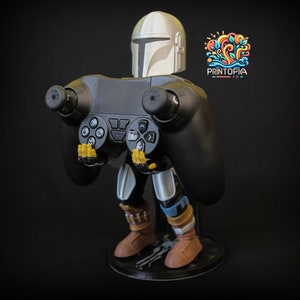May include: A black and gray video game controller stand featuring a character wearing a silver helmet and holding the controller. The character is standing on a black base with the word "PRINTOPIA" printed on it.