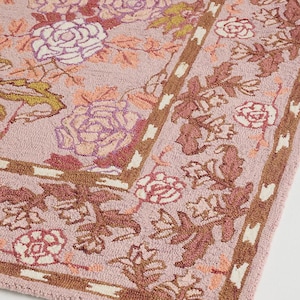 May include: A rectangular rug with a floral pattern in shades of pink, brown, and white. The rug features a repeating design of roses and leaves, with a border of brown and white accents. The rug is made of a soft, textured material.