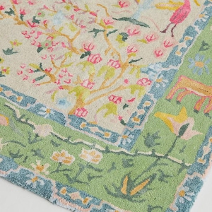 May include: A colorful rug with a floral and animal design. The rug features a cream-colored background with pink flowering trees, a tiger, and a pink bird. The border is green with blue accents and floral patterns.
