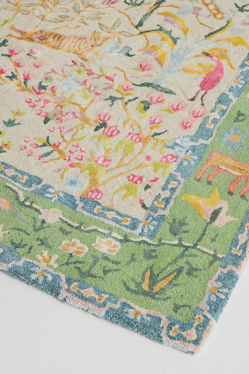 May include: A colorful rug with a floral and animal design. The rug features a cream-colored background with pink flowering trees, a tiger, and a pink bird. The border is green with blue accents and floral patterns.