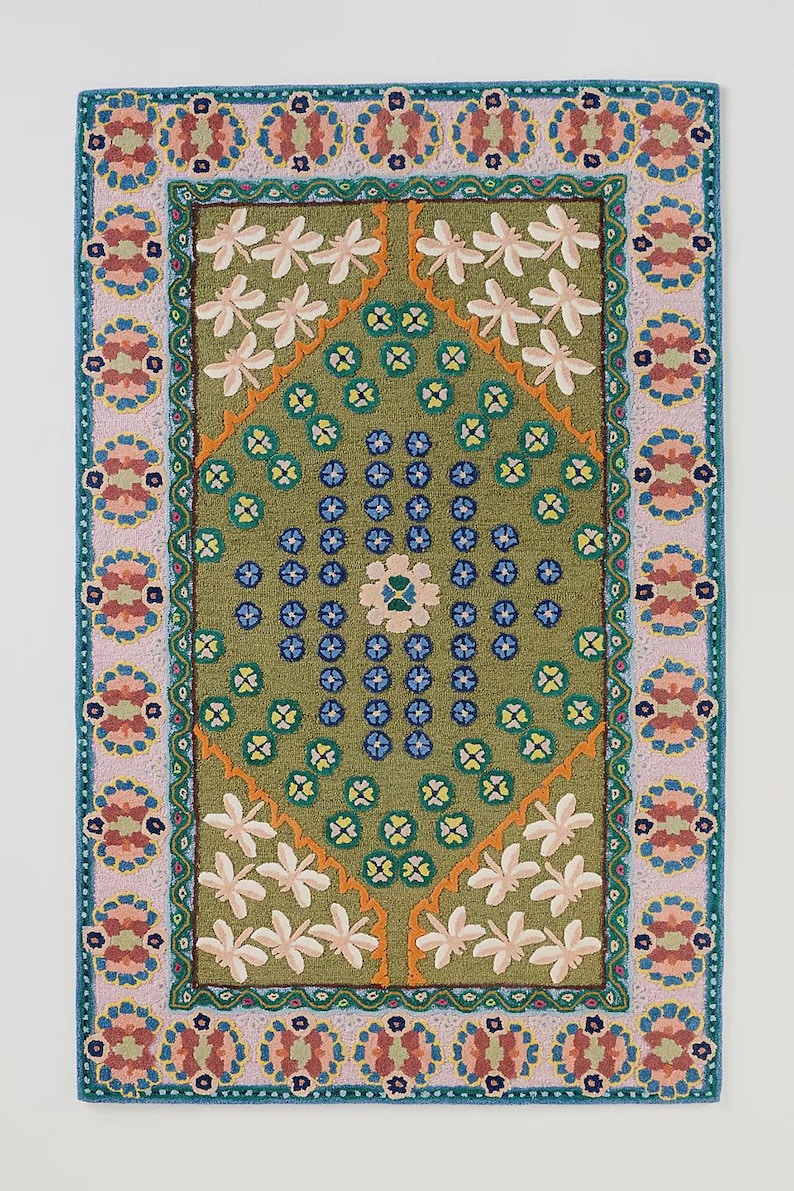 May include: A rectangular rug with a green center featuring white floral and blue accents. The rug has a pink and teal border with floral patterns. The rug's dimensions are approximately 24 x 36 inches.