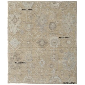 May include: Beige and gray patterned area rug with the text "RAAG CARPET" in multiple locations. The rug features a central diamond design and floral motifs. The rug is rectangular.