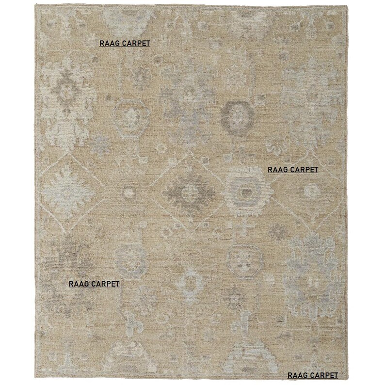 May include: Beige and gray patterned area rug with the text "RAAG CARPET" in multiple locations. The rug features a central diamond design and floral motifs. The rug is rectangular.