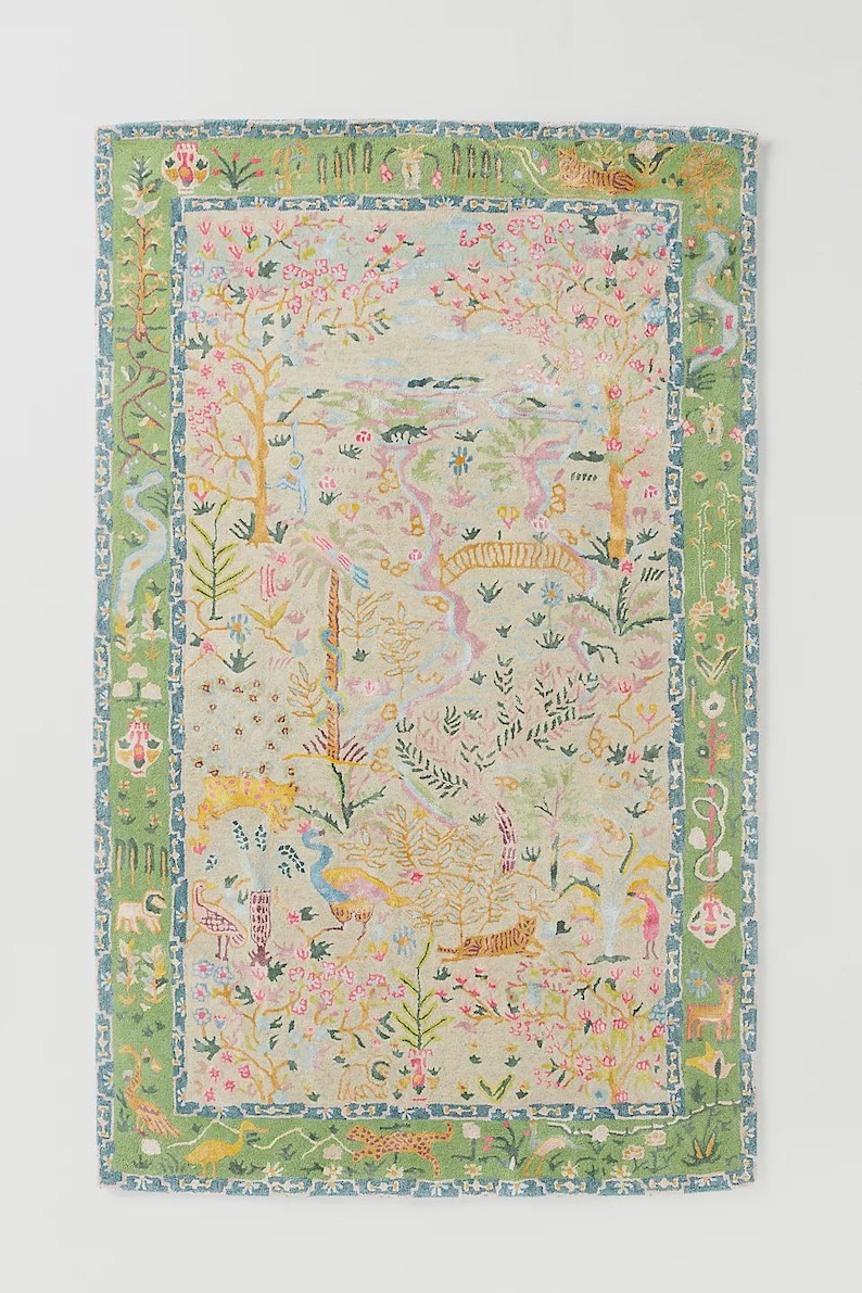 May include: A rectangular rug with a detailed, colorful design. The rug features a light green background with a central scene of trees, flowers, and animals in pink, yellow, and blue. A green border frames the design.