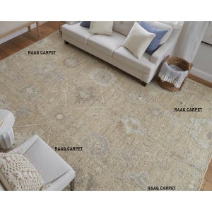 May include: Beige and gray patterned area rug with a distressed design. The rug is rectangular and covers a hardwood floor. A white sofa with pillows, a chair, and a basket are visible in the room. The text "RAAG CARPET" is printed on the rug.