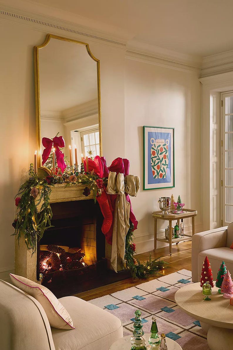 Puede incluir: Un sal&oacute;n festivo con una chimenea decorada, con un gran espejo con marco dorado. La repisa de la chimenea est&aacute; adornada con guirnaldas, velas y grandes lazos rosas. Una mesa auxiliar tiene bebidas y una impresi&oacute;n enmarcada.