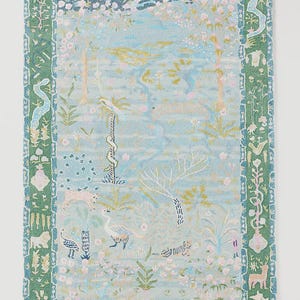 May include: A rectangular rug with a light blue background featuring a whimsical forest scene with trees, birds, and animals. The rug has a green border with decorative patterns. The design includes pink flowers and gold accents.