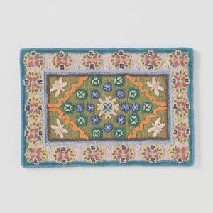 May include: Rectangular, hand-tufted rug with a floral design. The rug features a green center with blue, orange, and white floral accents. The border is light pink with yellow and red floral patterns, framed by a blue edge.