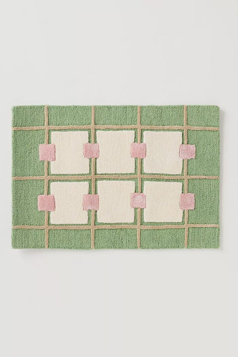 May include: A rectangular rug with a green background and a grid pattern. The grid is made of tan lines, with off-white squares and pink accents. The rug has a textured, woven appearance.