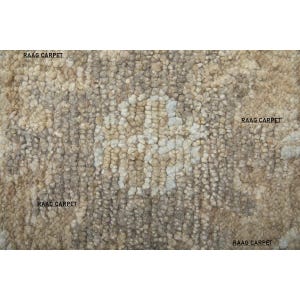 May include: A textured rug with a neutral color palette, featuring shades of beige, brown, and off-white. The surface has a nubby, looped texture, creating a visually interesting pattern. The words "RAAG CARPET" are printed on the rug.