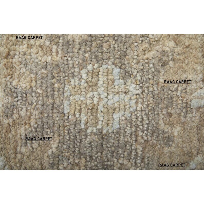 May include: A textured rug with a neutral color palette, featuring shades of beige, brown, and off-white. The surface has a nubby, looped texture, creating a visually interesting pattern. The words "RAAG CARPET" are printed on the rug.