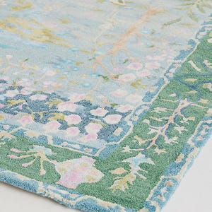 May include: A light blue rug with a floral design and a green border. The rug features a pattern of pink and yellow flowers, birds, and branches. The border is a darker green with a repeating leaf pattern.