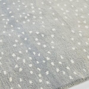 May include: A gray rug with a pattern of white, irregular spots. The rug has a soft, textured appearance and a gradient effect, transitioning from a darker gray to a lighter shade. The spots are scattered across the surface.
