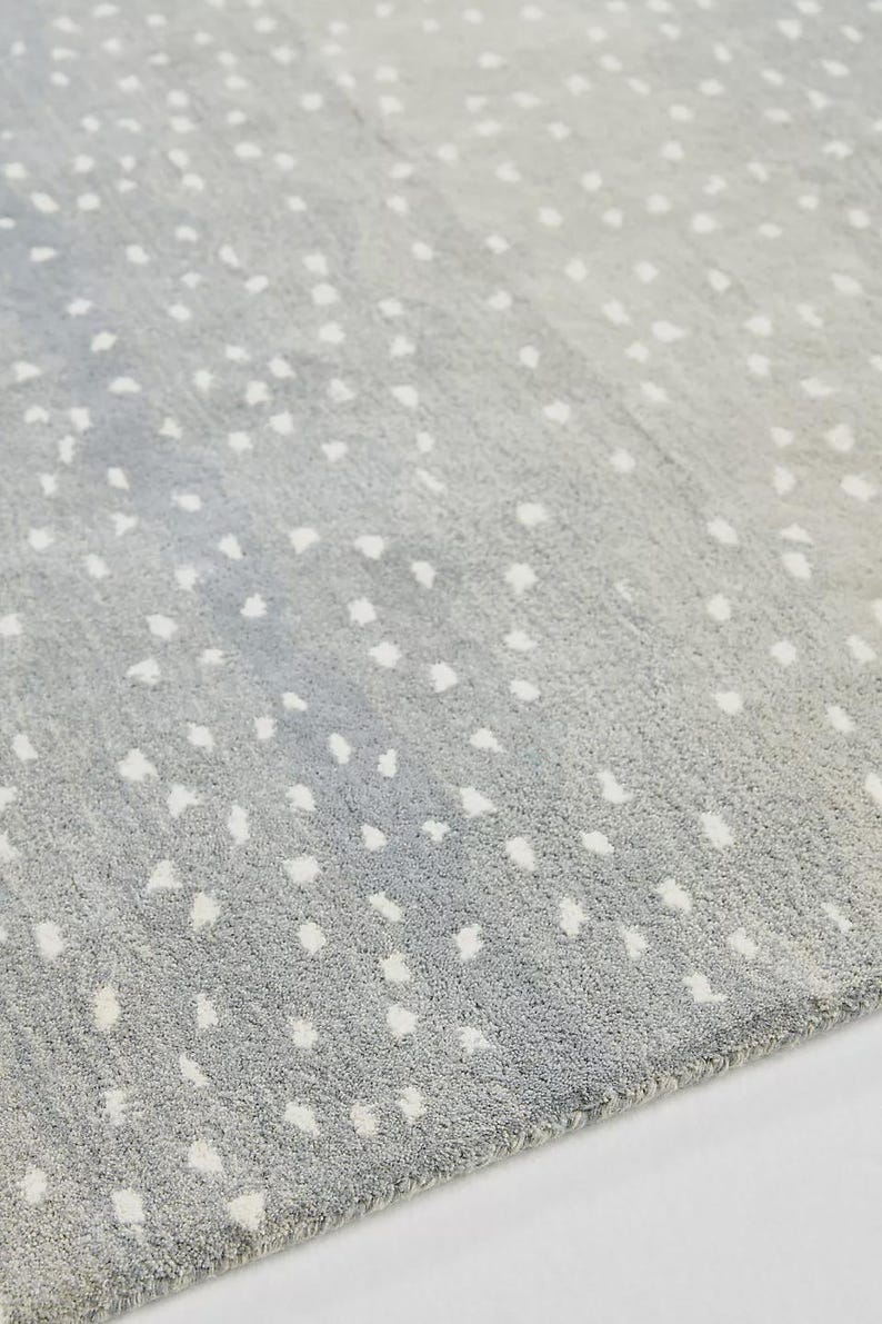 May include: A gray rug with a pattern of white, irregular spots. The rug has a soft, textured appearance and a gradient effect, transitioning from a darker gray to a lighter shade. The spots are scattered across the surface.
