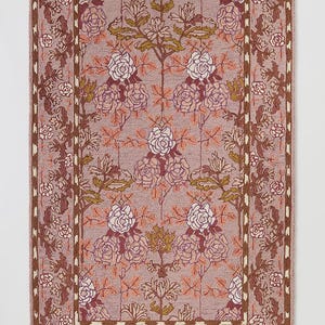 May include: Rectangular rug with a floral pattern in shades of mauve, brown, and cream. The design features stylized roses and foliage, framed by a border with repeating floral motifs. The rug's color palette is muted and elegant.